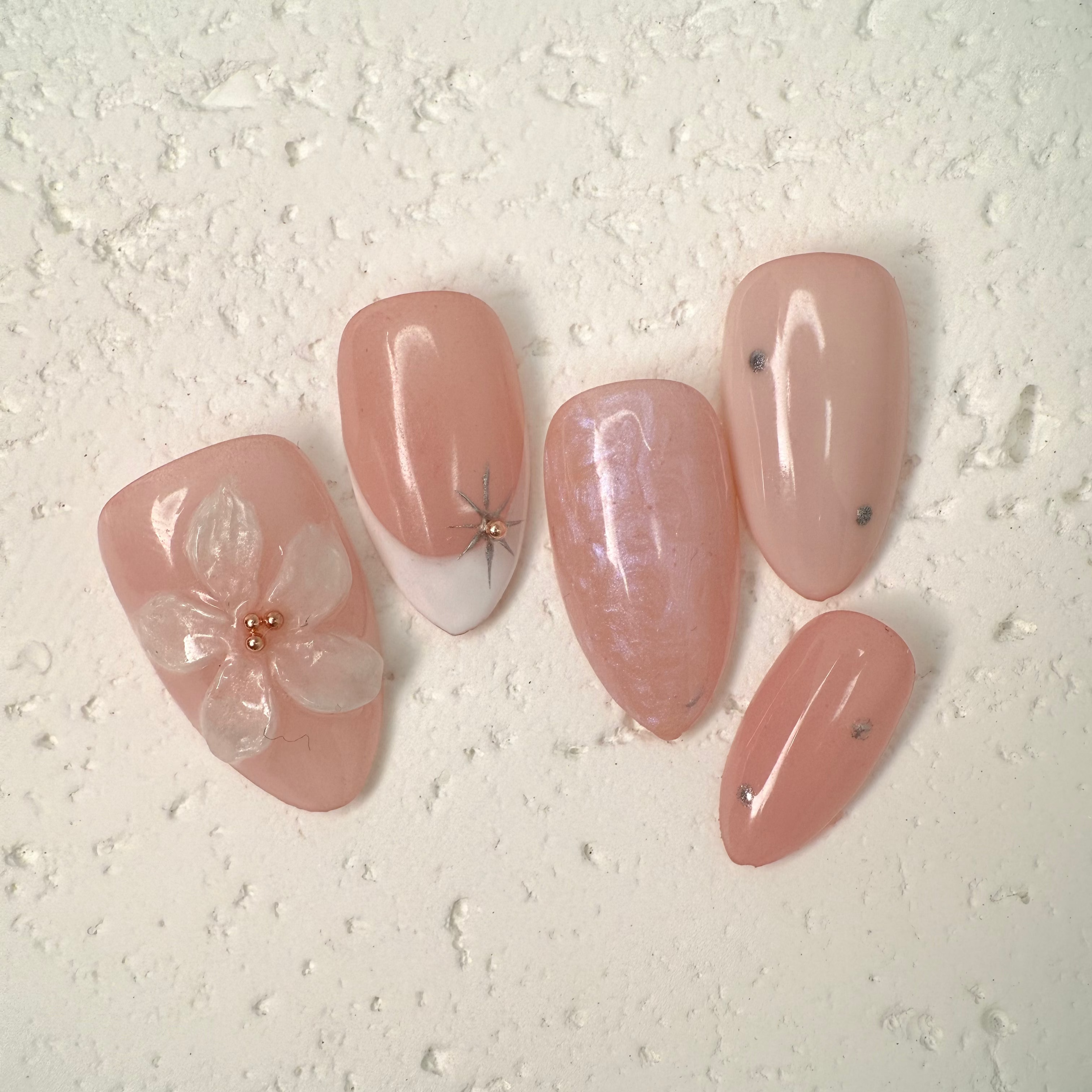 Close-up of nude press-on nails with 3D white floral design, gold outline, and soft marble accents, handcrafted for weddings and elegant events.