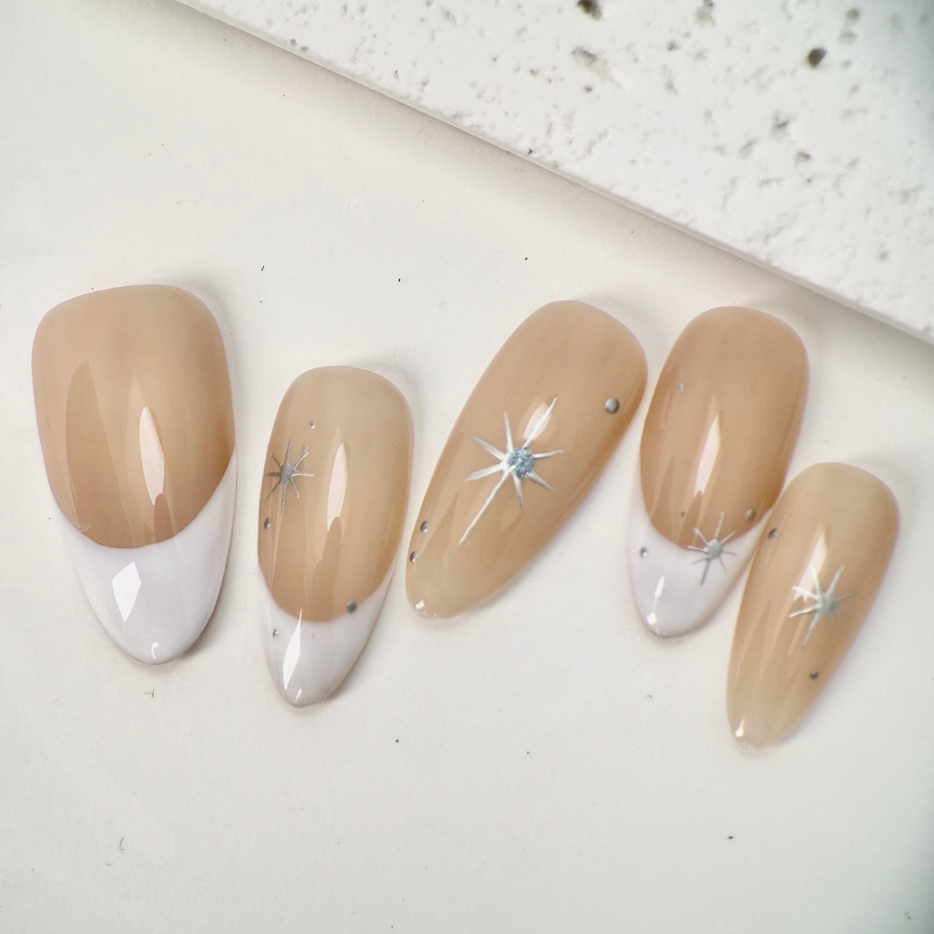 Close-up of nude French press-on nails with white tips, silver star accents, and small crystal details, handcrafted and reusable, ideal for elegant occasions.
