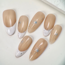 Close-up of nude French press-on nails with white tips, silver star accents, and small crystal details, handcrafted and reusable, ideal for elegant occasions.
