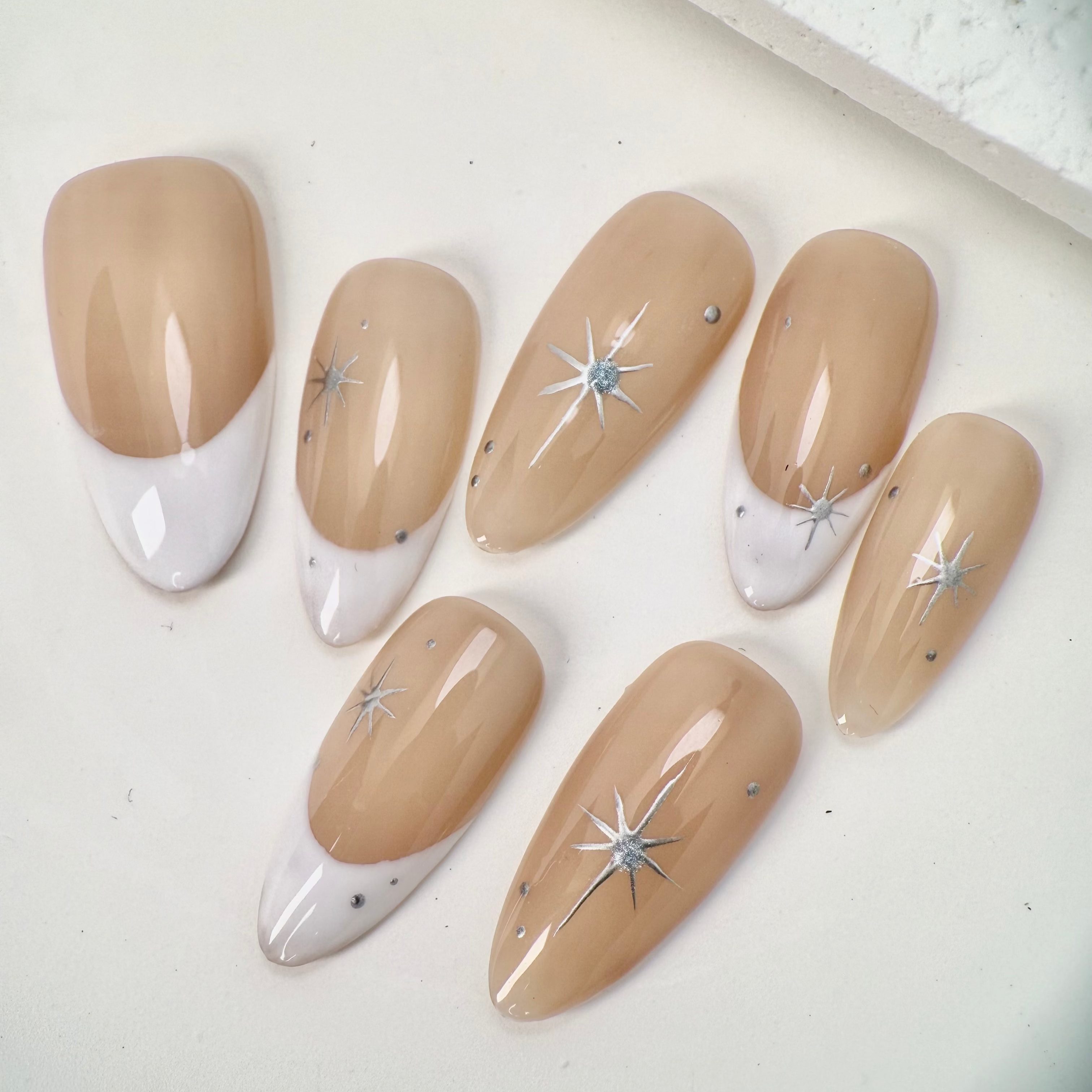 Close-up of nude French press-on nails with white tips, silver star accents, and small crystal details, handcrafted and reusable, ideal for elegant occasions.
