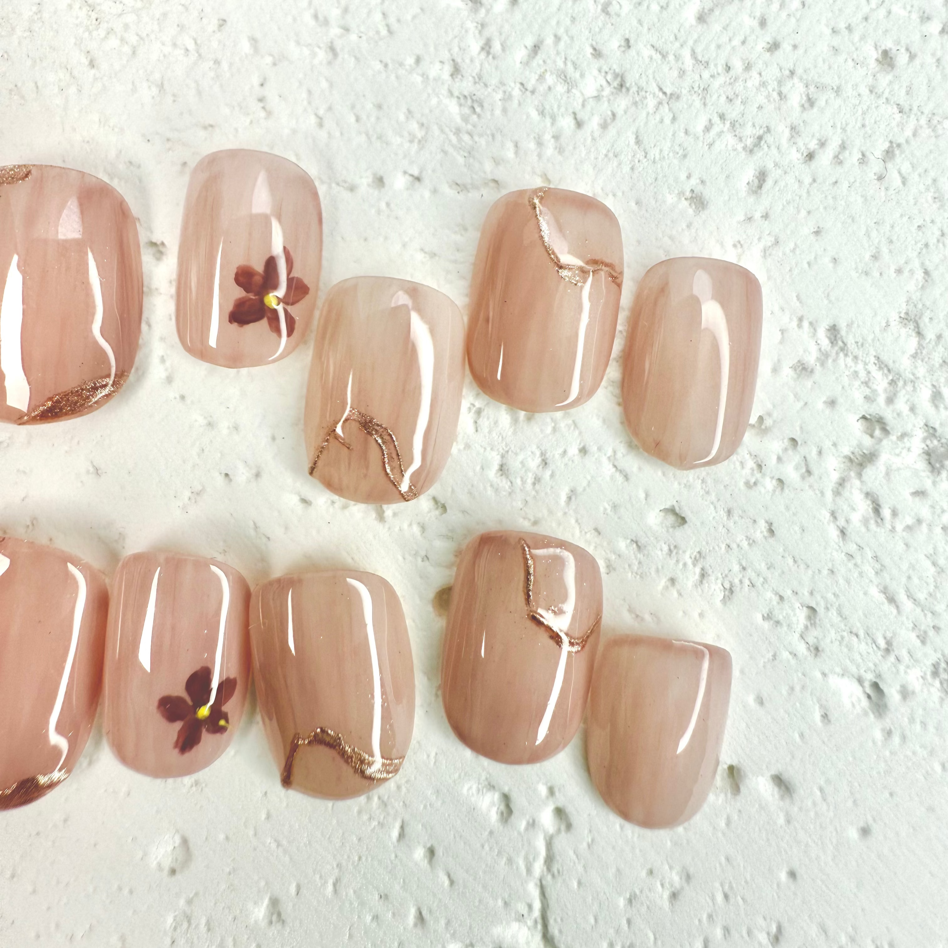 Close-up of blush nude pink press-on nails with small floral accents and gold marble lines, handcrafted for weddings and elegant occasions.