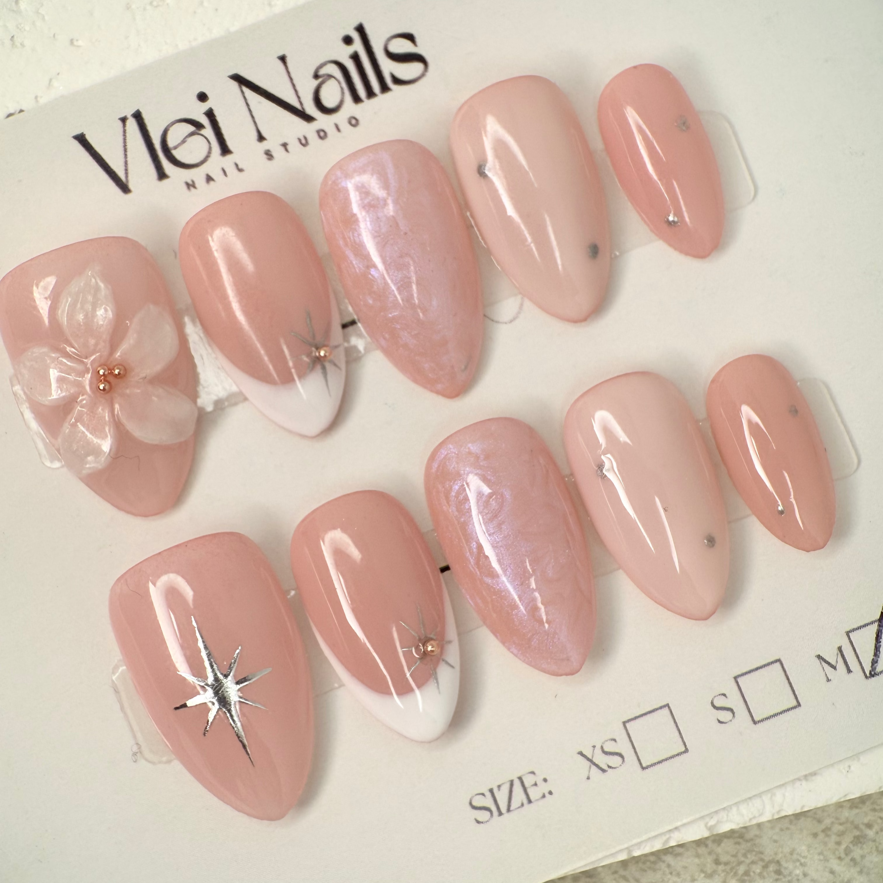 Close-up of nude press-on nails with 3D white floral design, gold outline, and soft marble accents, handcrafted for weddings and elegant events.