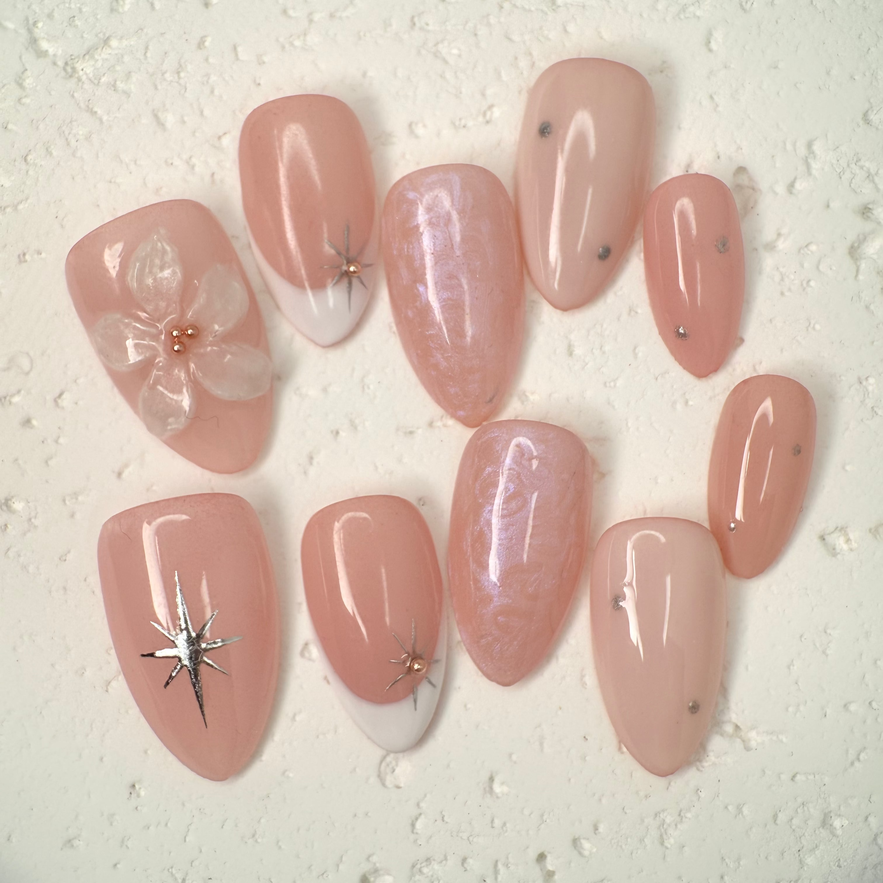 Close-up of nude press-on nails with 3D white floral design, gold outline, and soft marble accents, handcrafted for weddings and elegant events.