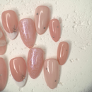 Close-up of nude press-on nails with 3D white floral design, gold outline, and soft marble accents, handcrafted for weddings and elegant events.