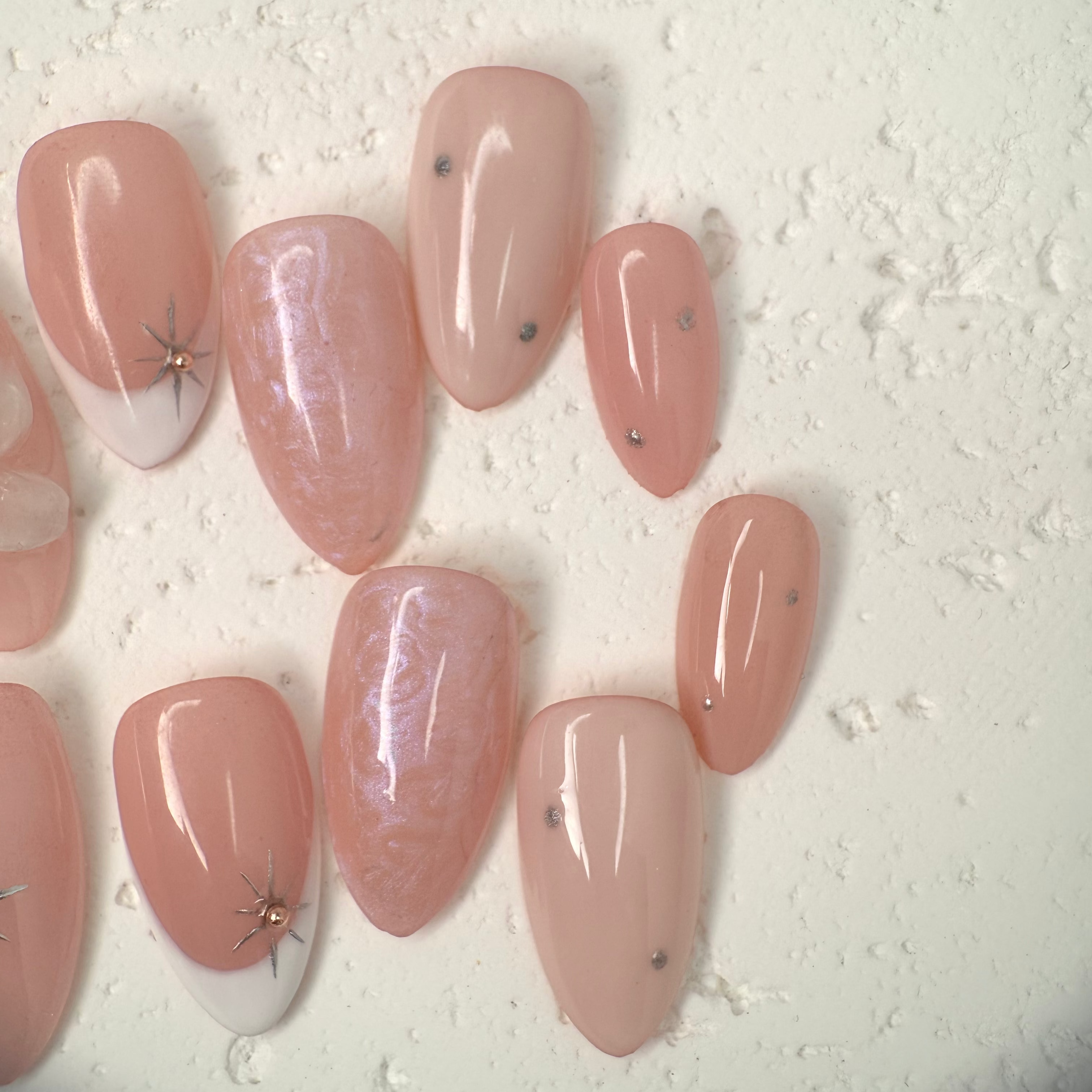 Close-up of nude press-on nails with 3D white floral design, gold outline, and soft marble accents, handcrafted for weddings and elegant events.