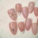 Close-up of nude press-on nails with 3D white floral design, gold outline, and soft marble accents, handcrafted for weddings and elegant events.