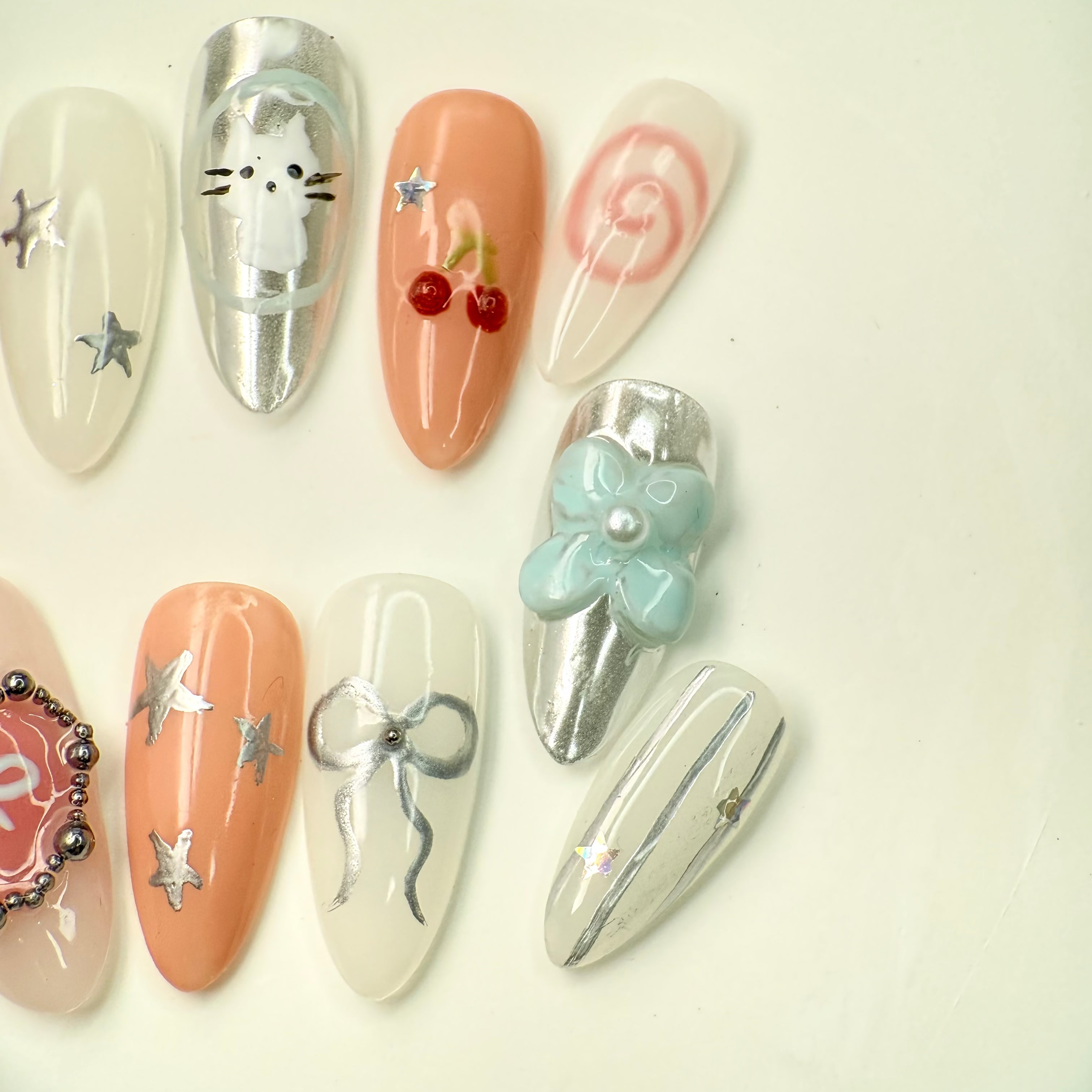 3D jelly bear and ribbon themed press-on nails in silver, pink, and nude tones with stars, cherries, and metallic heart details – handcrafted by Vlei Nails Cape Town.
