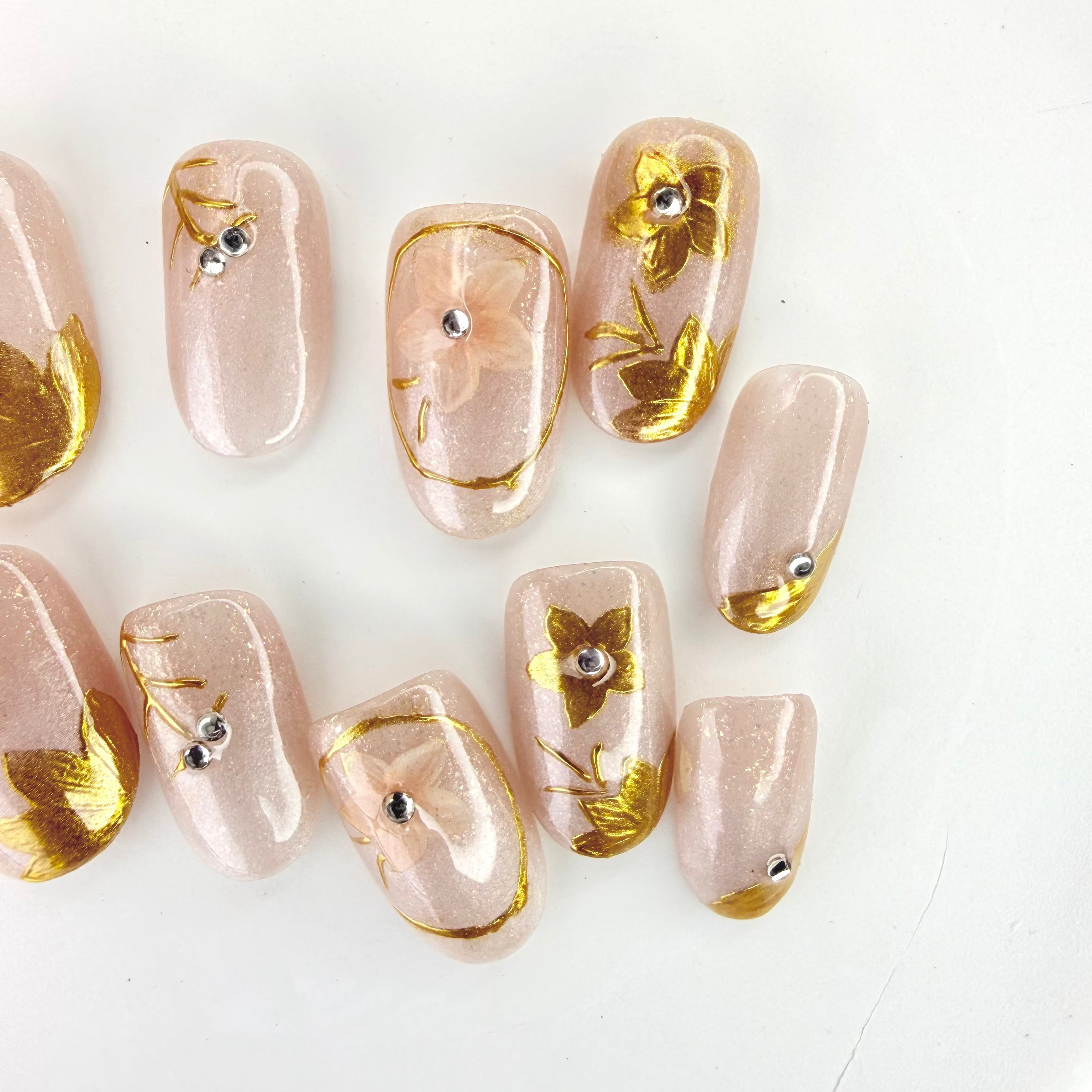 Handcrafted nude and silver press-on nails with 3D gold glitter flower design and metallic shimmer – made by Vlei Nails Cape Town.
