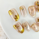 Handcrafted nude and silver press-on nails with 3D gold glitter flower design and metallic shimmer – made by Vlei Nails Cape Town.
