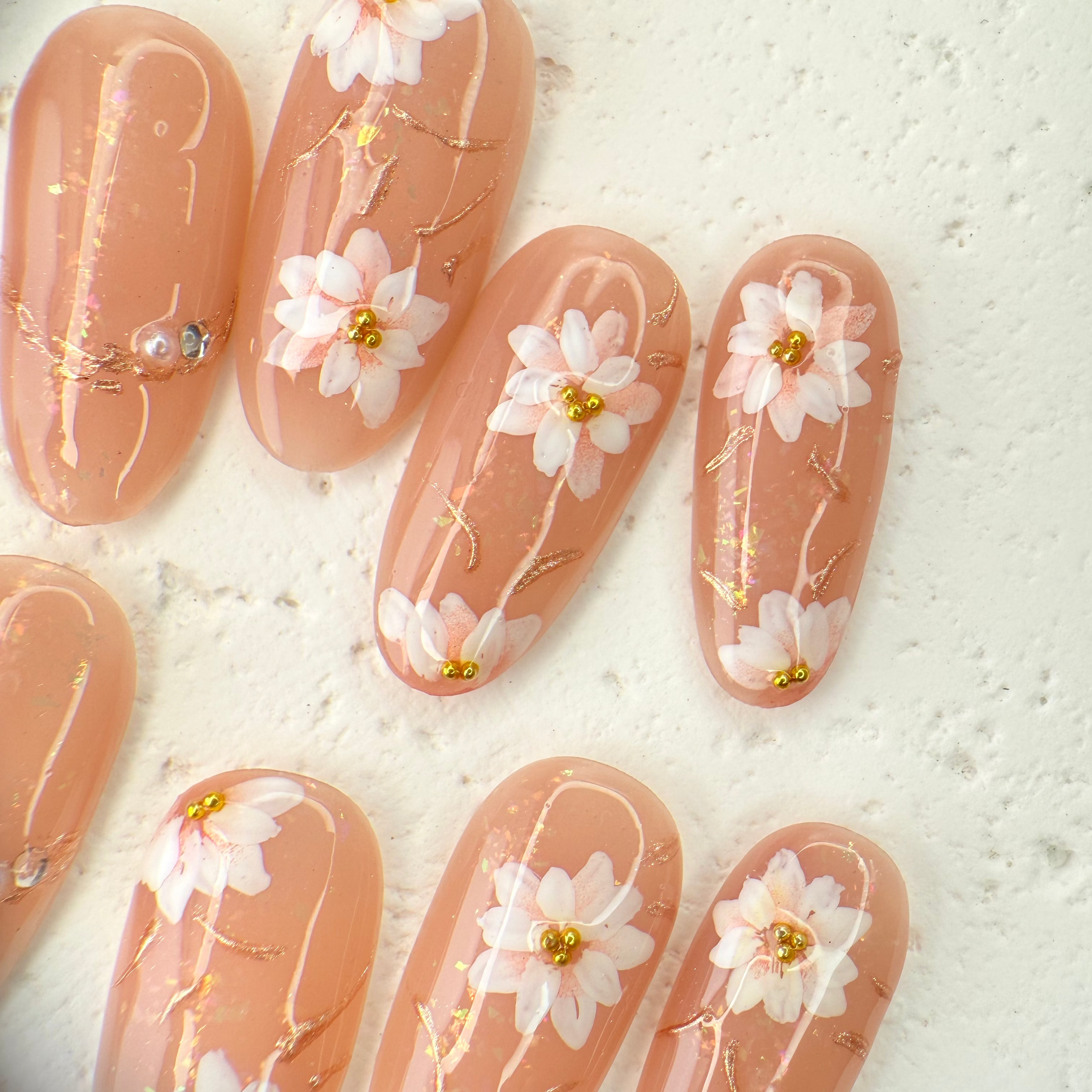 Handcrafted nude pink press-on nails with 3D pearl flowers and gold foil shimmer – made by Vlei Nails Cape Town.
