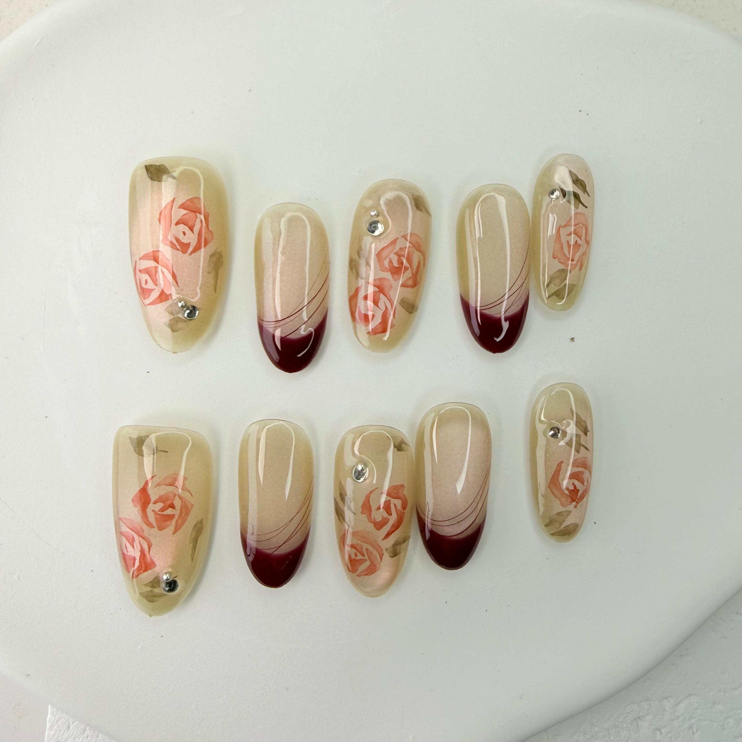 Handcrafted nude press-on nails with red French tips and 3D pink rose accents – made by Vlei Nails Cape Town.

