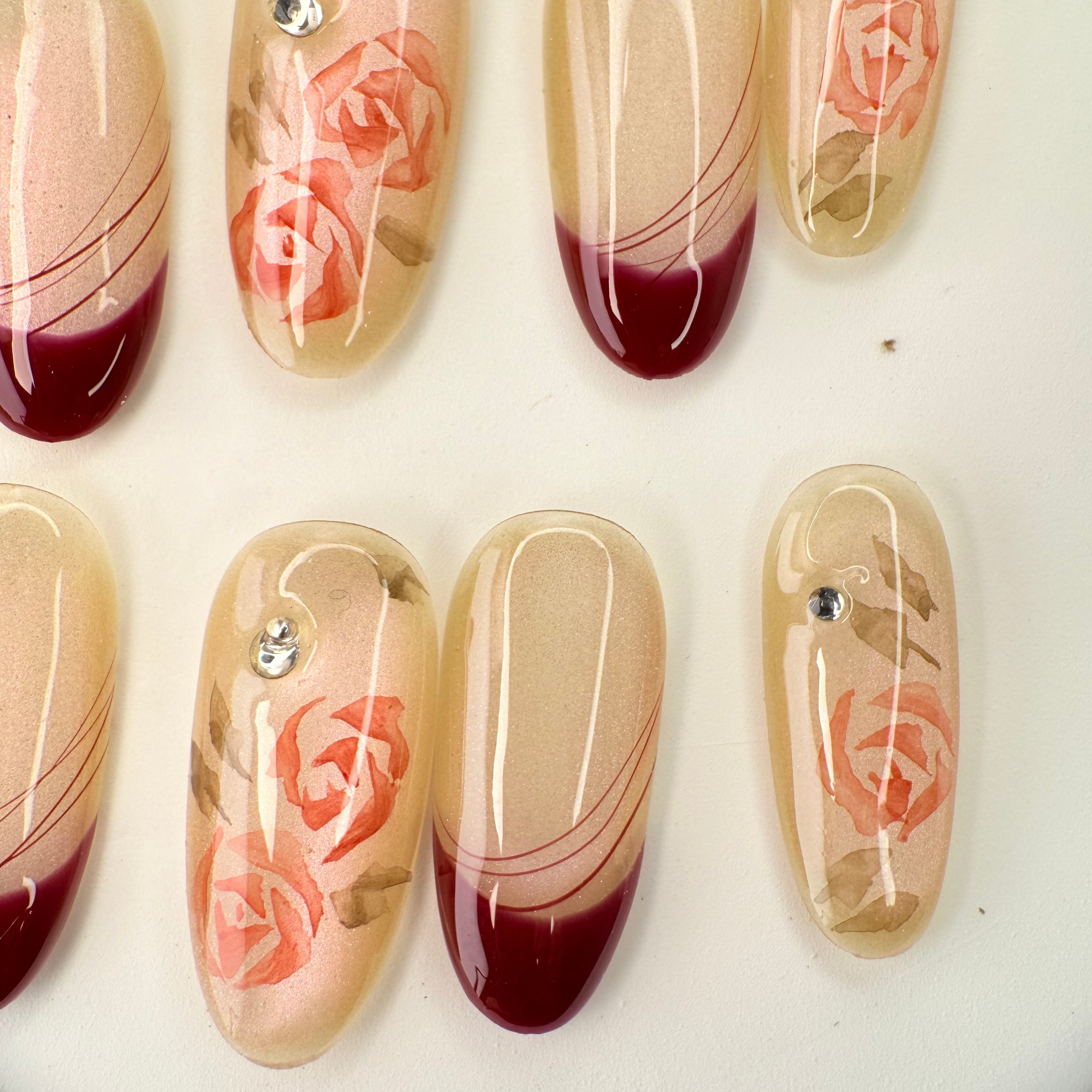 Handcrafted nude press-on nails with red French tips and 3D pink rose accents – made by Vlei Nails Cape Town.
