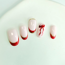 Handcrafted nude press-on nails with red and gold French tips and a red ribbon accent, designed by Vlei Nails Cape Town.