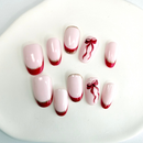 Handcrafted nude press-on nails with red and gold French tips and a red ribbon accent, designed by Vlei Nails Cape Town.