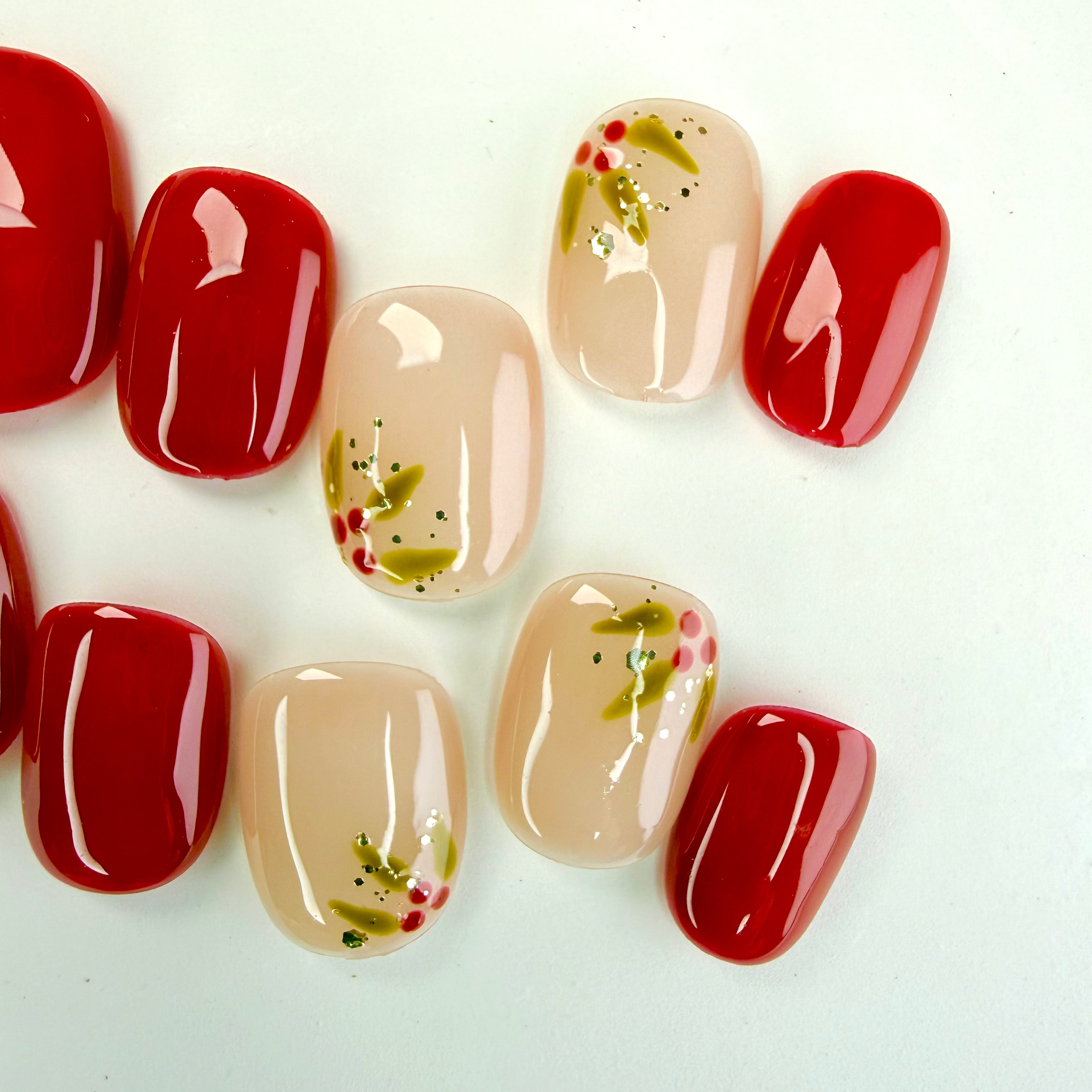Christmas press-on nails with red and nude tones, decorated with hand-painted holly leaves and berries — festive handmade holiday nails by Vlei Nails.
