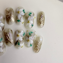 Handcrafted green marble press-on nails with white 3D floral designs and gold foil accents.