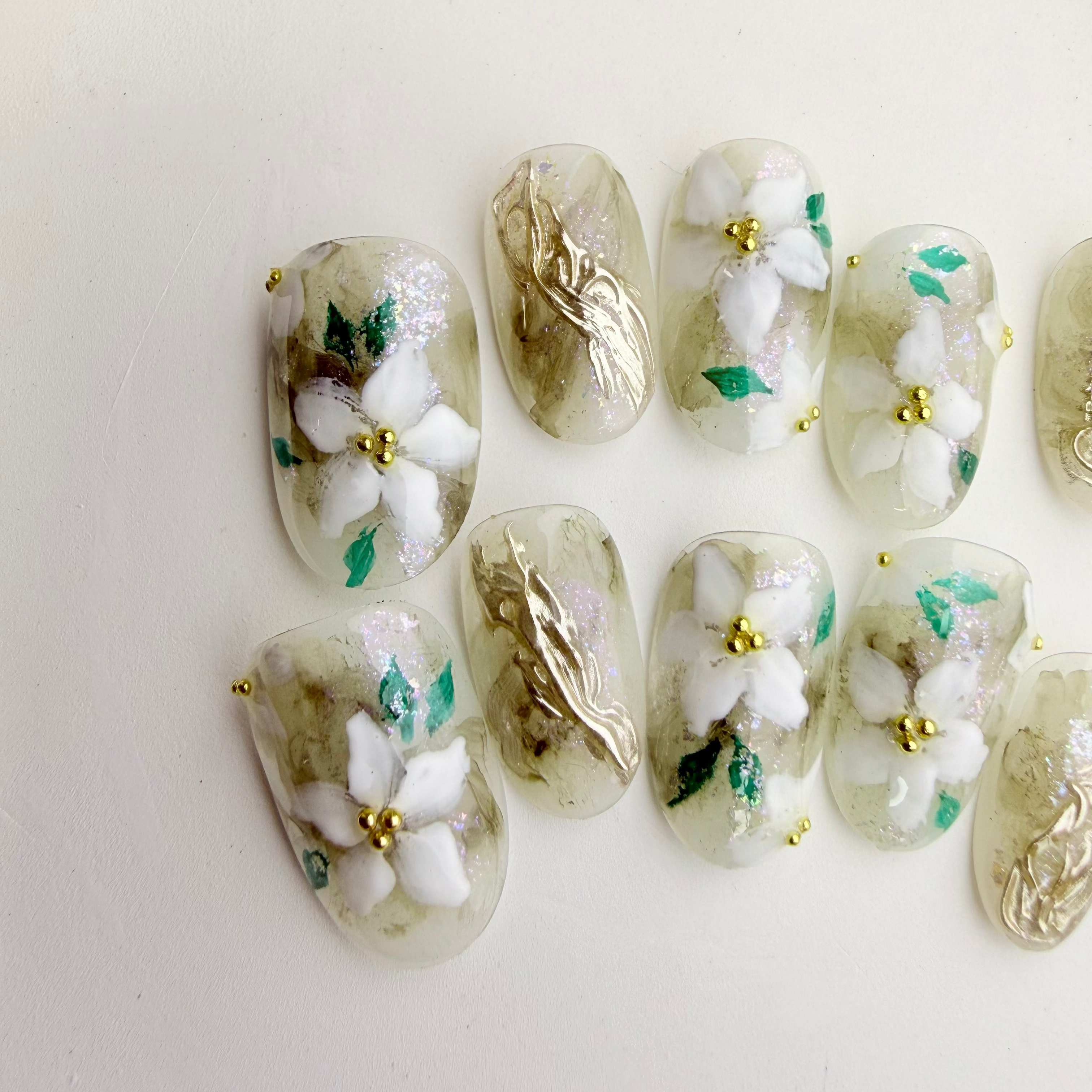 Handcrafted green marble press-on nails with white 3D floral designs and gold foil accents.