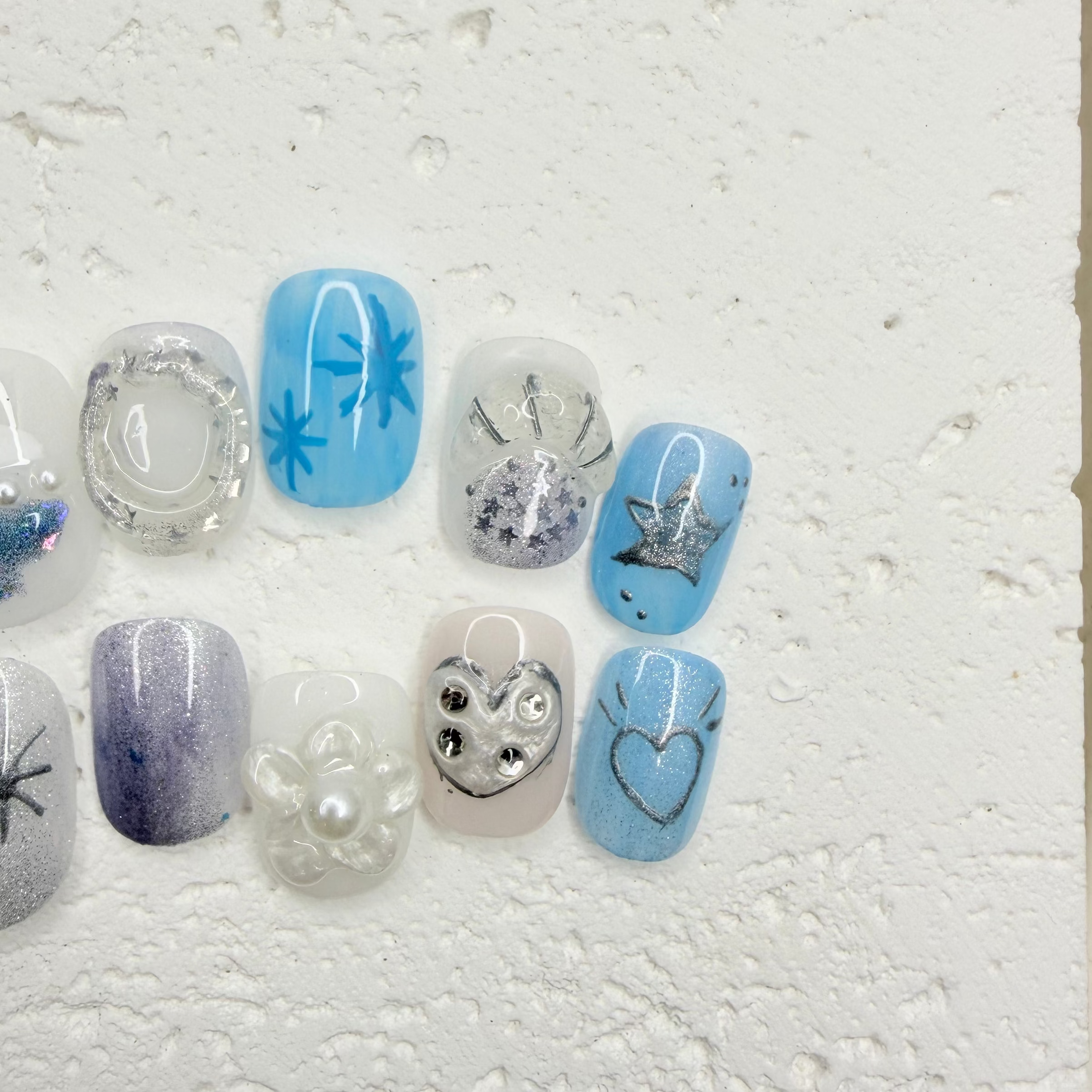 Icy blue and silver press-on nail set with starburst designs, glitter accents, pearls, rhinestones, and a heart outline nail.