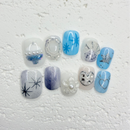 Icy blue and silver press-on nail set with starburst designs, glitter accents, pearls, rhinestones, and a heart outline nail.