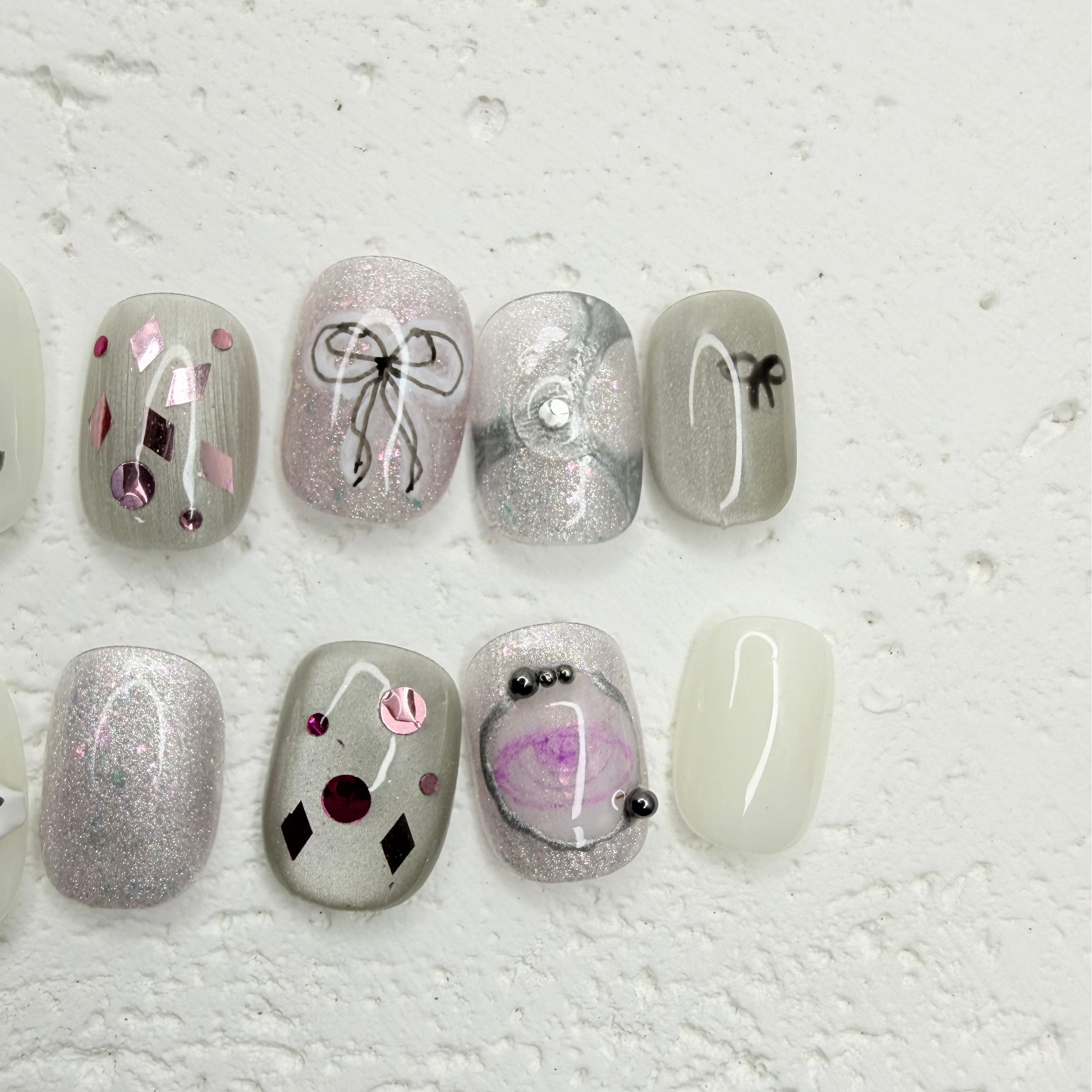 Grey press-on nails with bow design, silver shimmer gel, crystal embellishments, pearl flower accent and artistic candle nail art