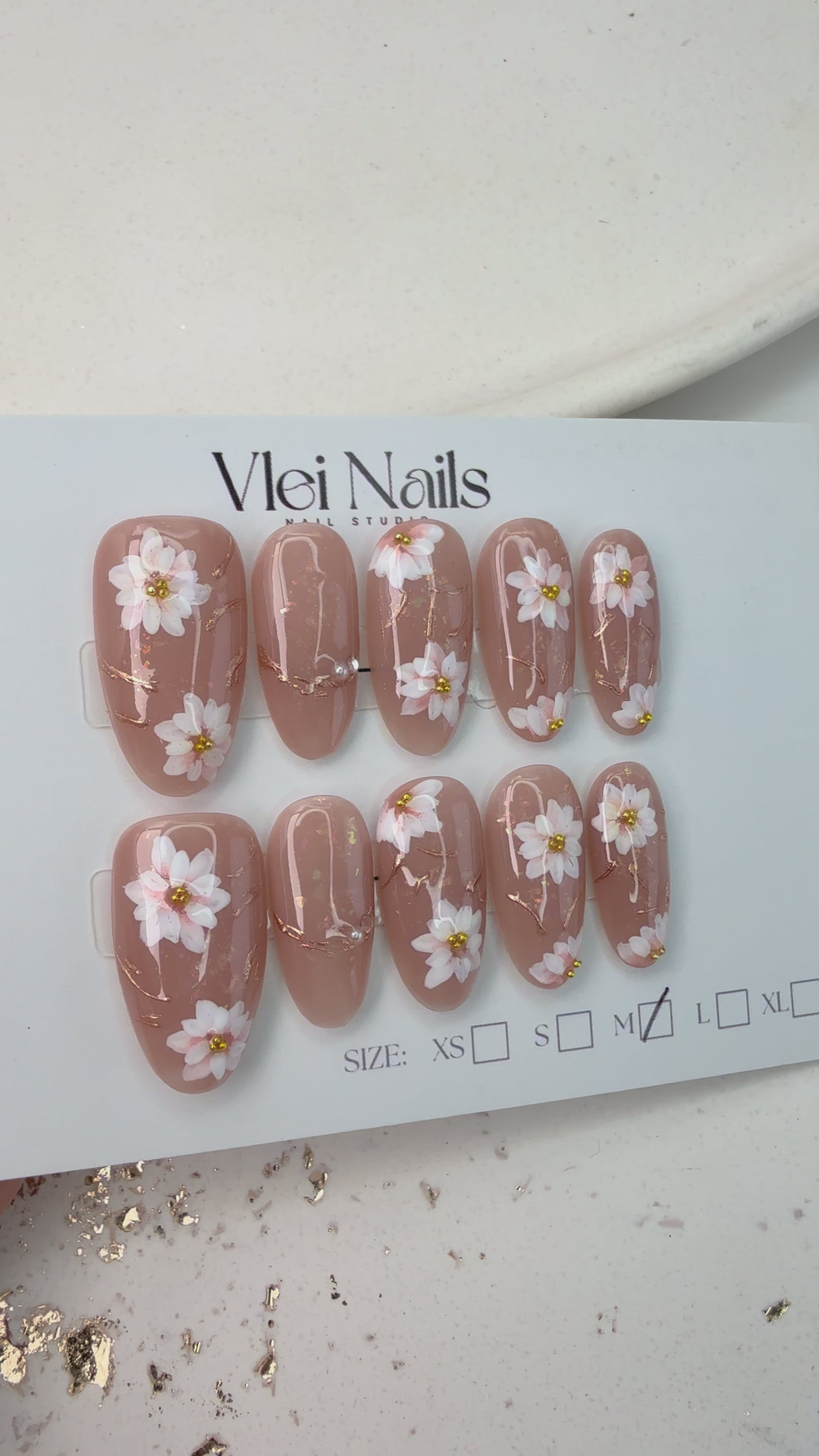 Handcrafted nude pink press-on nails with 3D pearl flowers and gold foil shimmer – made by Vlei Nails Cape Town.
