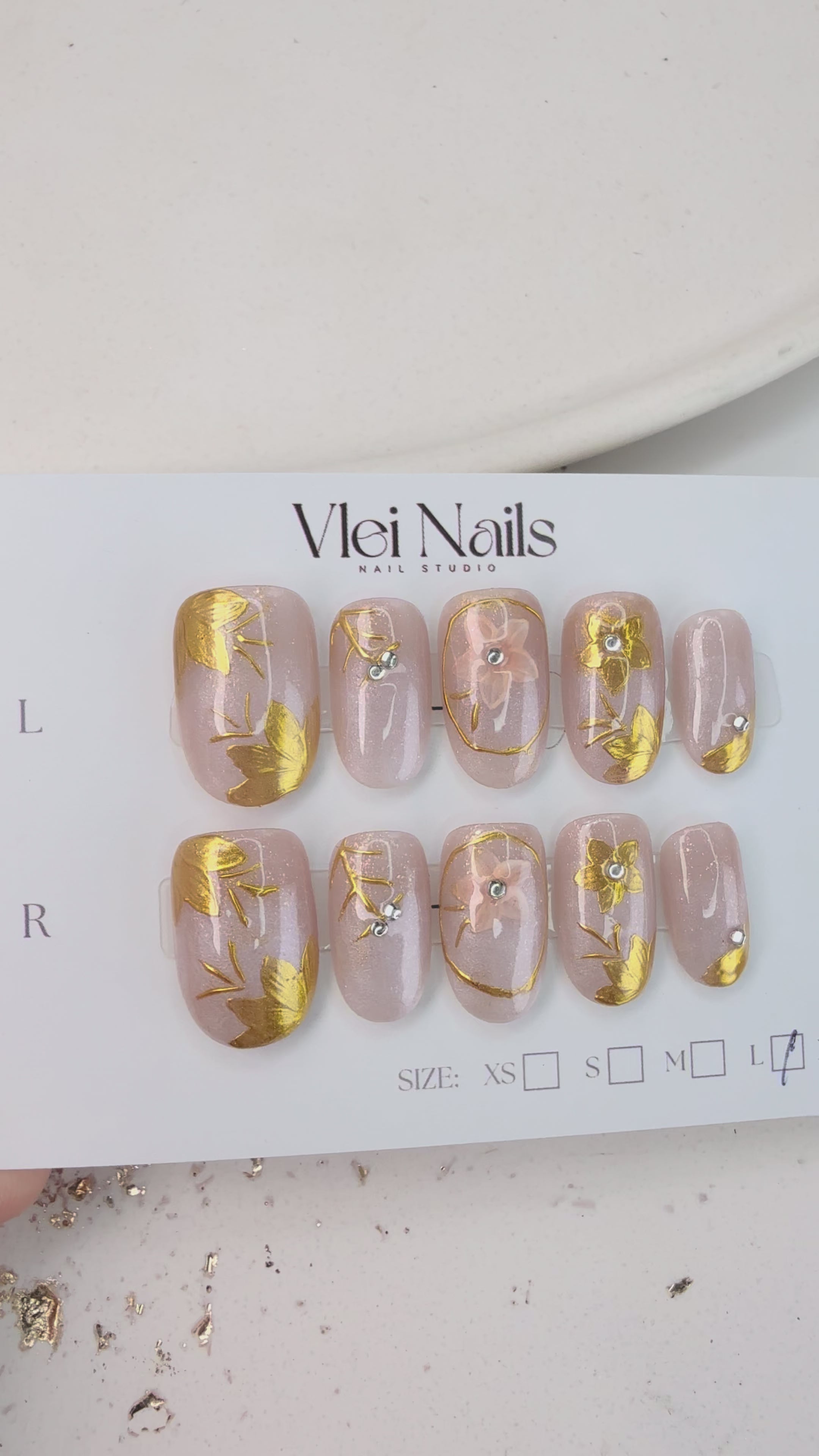 Handcrafted nude and silver press-on nails with 3D gold glitter flower design and metallic shimmer – made by Vlei Nails Cape Town.
