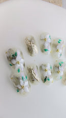 Handcrafted green marble press-on nails with white 3D floral designs and gold foil accents.