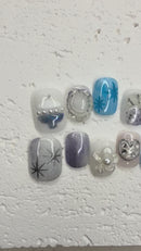 Icy blue and silver press-on nail set with starburst designs, glitter accents, pearls, rhinestones, and a heart outline nail.